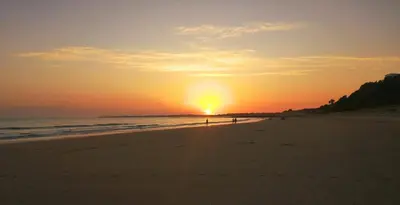 a sunset on the beach with people walking on the beach at GATU PREMIUM Villa Aramburu, 