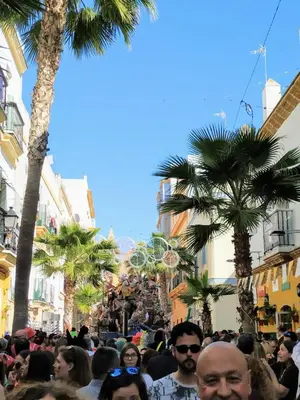 a crowd of people walking down a street with palm trees at La Casa del Arte in Cádiz
