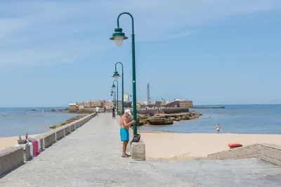a man standing on a pier next to the beach at BARQUILLAS de la Caleta Home by Cadiz4Rentals in Cádiz