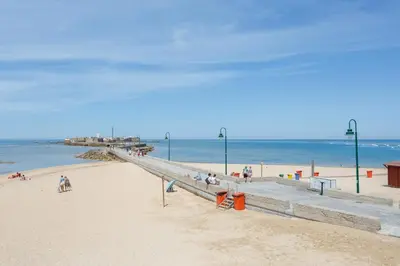a group of people sitting on a beach near the ocean at BARQUILLAS de la Caleta Home by Cadiz4Rentals in Cádiz