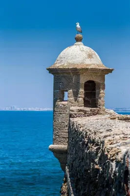 a stone tower on the side of a wall next to the ocean at Jano PuertaTierra in Cádiz