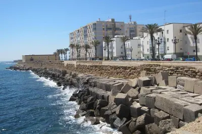 a stone wall next to the ocean with buildings at Jano PuertaTierra in Cádiz