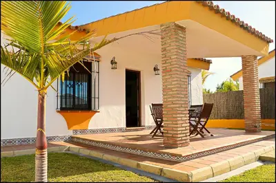 a house with a patio with chairs and a palm tree at Chalet con piscina privada in Conil de la Frontera