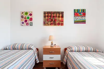 a bedroom with two beds and a nightstand and paintings at Casa Huerta del Pitorreo in Conil de la Frontera