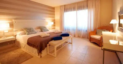 a bedroom with a bed and a chair and a window at Aparthotel Novo Resort in Chiclana de la Frontera