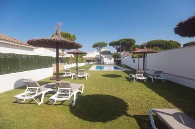 a group of lawn chairs and umbrellas next to a pool at Villas La Barrosa in Chiclana de la Frontera