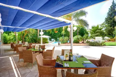 a patio with tables and chairs under a blue umbrella at Hipotels Sherry Park in Jerez de la Frontera
