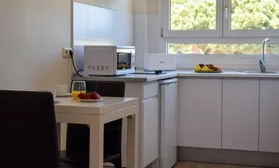 a kitchen with white cabinets and a table with a microwave at Aparthotel Novo Sancti Petri in Chiclana de la Frontera