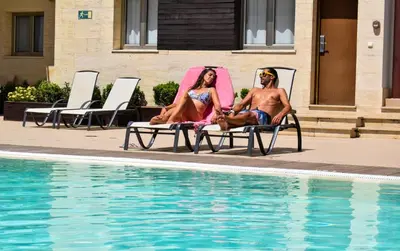 two people sitting in lawn chairs next to a swimming pool at Aparthotel Novo Sancti Petri in Chiclana de la Frontera