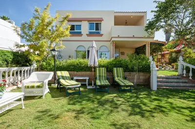 a house with chairs and an umbrella in the yard at Charming villa in Sanlúcar de Barrameda with private pool in Sanlúcar de Barrameda