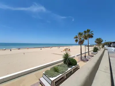 a beach with benches and palm trees and the ocean at Apartamento Sea Views Rota in Rota