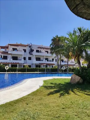 a large apartment building with a swimming pool and palm trees at APARTAMENTO EN COTO DE SANCTI PETRI in Chiclana de la Frontera