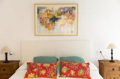 a bed with two red pillows and a painting above it at Apartamentos Homing Puerto Sherry in El Puerto de Santa María