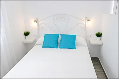 a bedroom with a white bed with blue pillows at Bungalow Ramos III in Conil de la Frontera