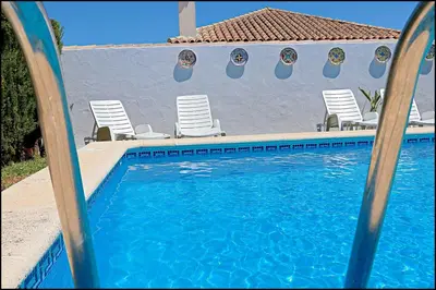 a swimming pool with chairs next to a house at Bungalow Ramos III in Conil de la Frontera
