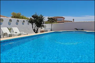 a swimming pool with two chairs and a wall at Bungalow Ramos III in Conil de la Frontera