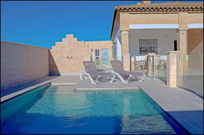 a swimming pool with two chairs next to a house at Chalet Peñuelas con piscina in Conil de la Frontera