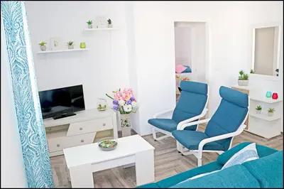 a living room with blue chairs and a tv at Chalet Ermita in Conil de la Frontera