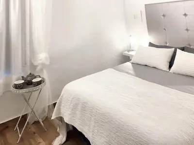 a white bedroom with a bed and a side table at Charming House + Chiclana de la Frontera + Garden in Chiclana de la Frontera