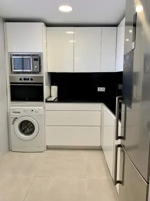 a white kitchen with a washer and a microwave at Duplex a 3 minutos de playa de la victoria Cadiz in Cádiz