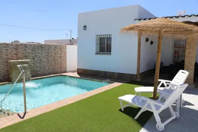 a swimming pool with two chairs and an umbrella at Chalet carril de los pareja in Conil de la Frontera