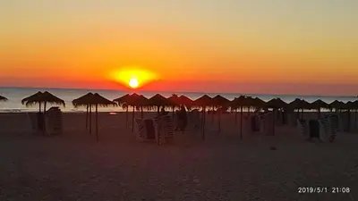a sunset on the beach with umbrellas and the ocean at Loft 500 metros de la playa in Cádiz