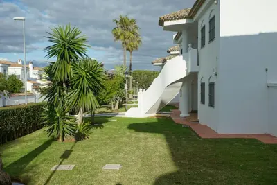 a yard with palm trees and a white house at LA BARROSA-NOVO SANCTI PETRI, wifi, aire acondicionado, parking in Chiclana de la Frontera