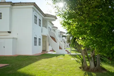 a row of white buildings with trees in the yard at LA BARROSA-NOVO SANCTI PETRI, wifi, aire acondicionado, parking in Chiclana de la Frontera