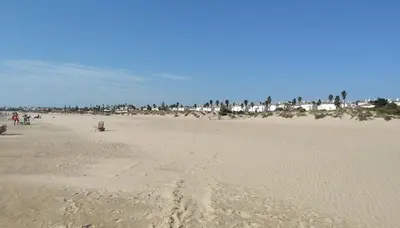 a beach with a group of people walking on the sand at Apartamento La Barrosa - Chiclana - Urb. Pinar Atlántico in Chiclana de la Frontera