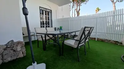 a patio with a table and chairs on the grass at Apartamento La Barrosa - Chiclana - Urb. Pinar Atlántico in Chiclana de la Frontera
