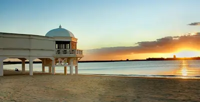 a building on the beach with the sunset in the background at Apartamento Centro de Cádiz y Playa in Cádiz
