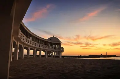 a building on the beach with a sunset in the background at Apartamento Centro de Cádiz y Playa in Cádiz