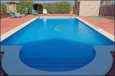 a large blue swimming pool with two chairs and a table at Apartamento con piscina comunitaria in Conil de la Frontera