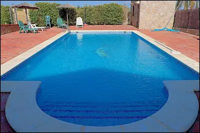 a large blue swimming pool with chairs and a table at Apartamento en complejo con piscina in Conil de la Frontera