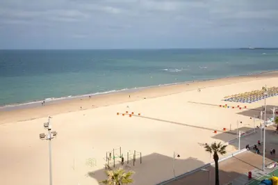 a beach with a lot of people and the ocean at Sunset Victoria Beach in Cádiz