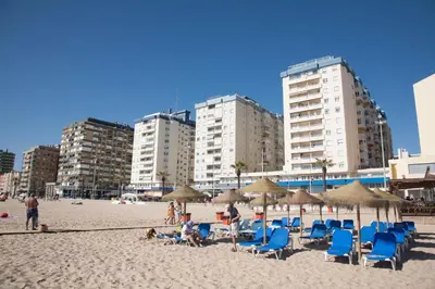 people on a beach with chairs and umbrellas and buildings at Sunset Victoria Beach in Cádiz