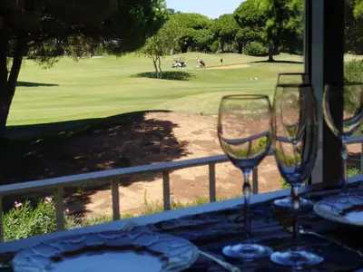 two wine glasses on a table with a view of a golf course at Indo en OGGOB com in Chiclana de la Frontera