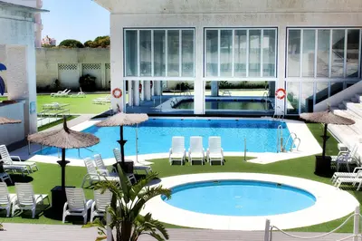 a large swimming pool in a building with chairs and umbrellas at Suites Puerto Sherry in El Puerto de Santa María