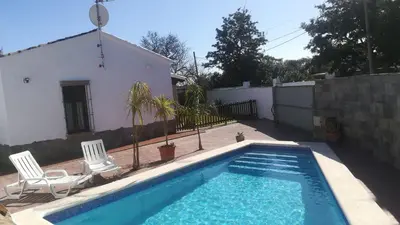 a swimming pool with two chairs and a house at Cortijo El Almendro, Urb. Fuente del Gallo, Conil in Conil de la Frontera
