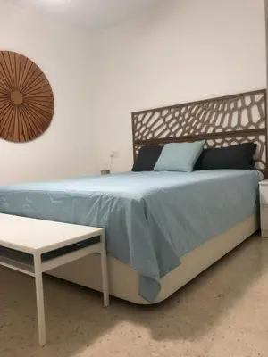 a bed with a blue comforter and a table at Masai Victoria Beach. A 100 metros de la playa. in Cádiz