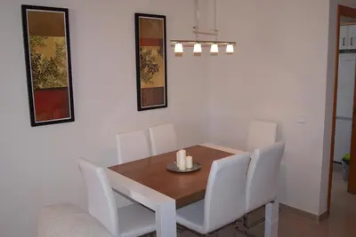 a dining room with a wooden table and white chairs at Costa Ballena Cómodo Bajo con Piscina, Patio y 3 Dormitorios Parking free in Rota