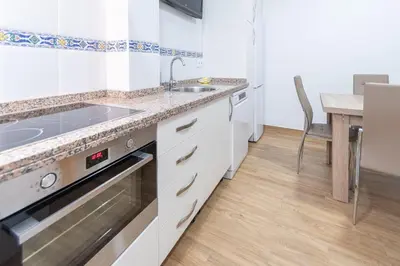a kitchen with white cabinets and a sink and a table at La casa de las margaritas in Cádiz