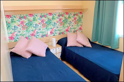 two beds in a room with blue sheets and pink pillows at Bungalow con piscina privada in Conil de la Frontera