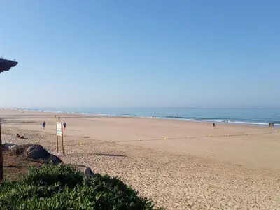 a beach with people walking on the sand and the ocean at Victoria Chipiona Unifamiliar in Chipiona