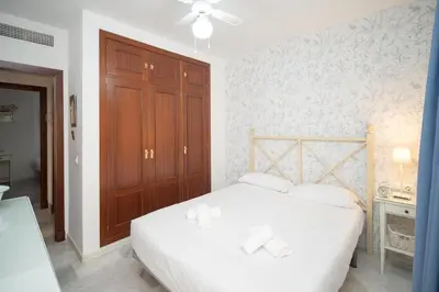 a bedroom with a white bed and a wooden cabinet at Sol y Vida, Apartamentos Living Sur in Sanlúcar de Barrameda