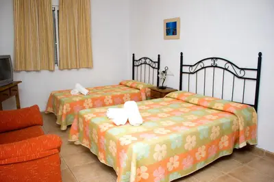 a room with two beds and a chair and a tv at Villa la Dehesa in Conil de la Frontera