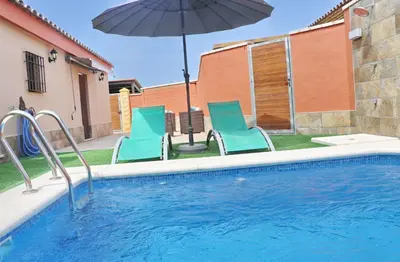 a swimming pool with two chairs and an umbrella at Chalet Sultan con piscina in Conil de la Frontera