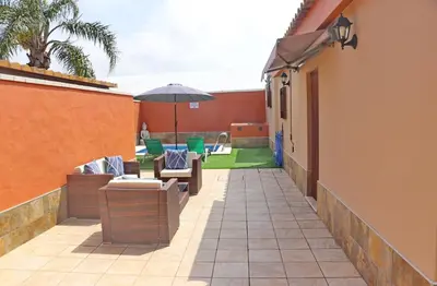 a patio with tables and chairs and an umbrella at Chalet Sultan con piscina in Conil de la Frontera