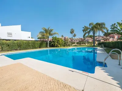 a large blue swimming pool with palm trees and houses at Holiday Home Brisamar - Novo Sancti Petri by Interhome in Chiclana de la Frontera