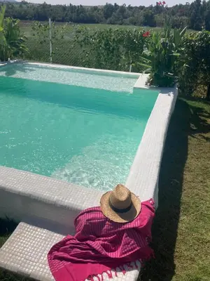 a woman in a pink dress sitting on a bench next to a swimming pool at El Lagar de los Abuelos in Arcos de la Frontera